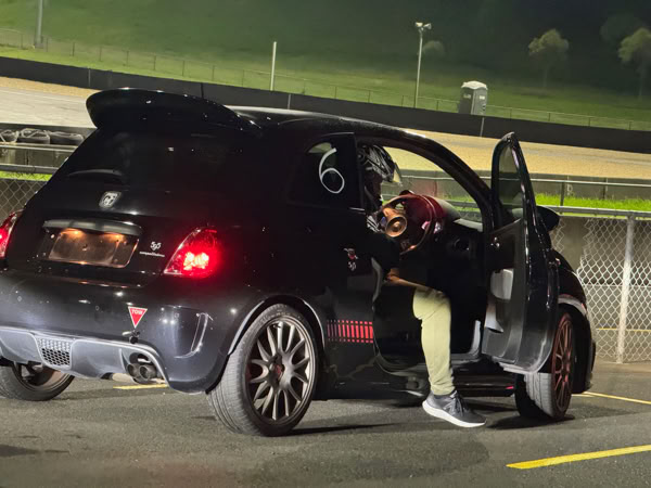 Fiat Abarth driver relaxing in the pits with the door open after completing a spirited track session.